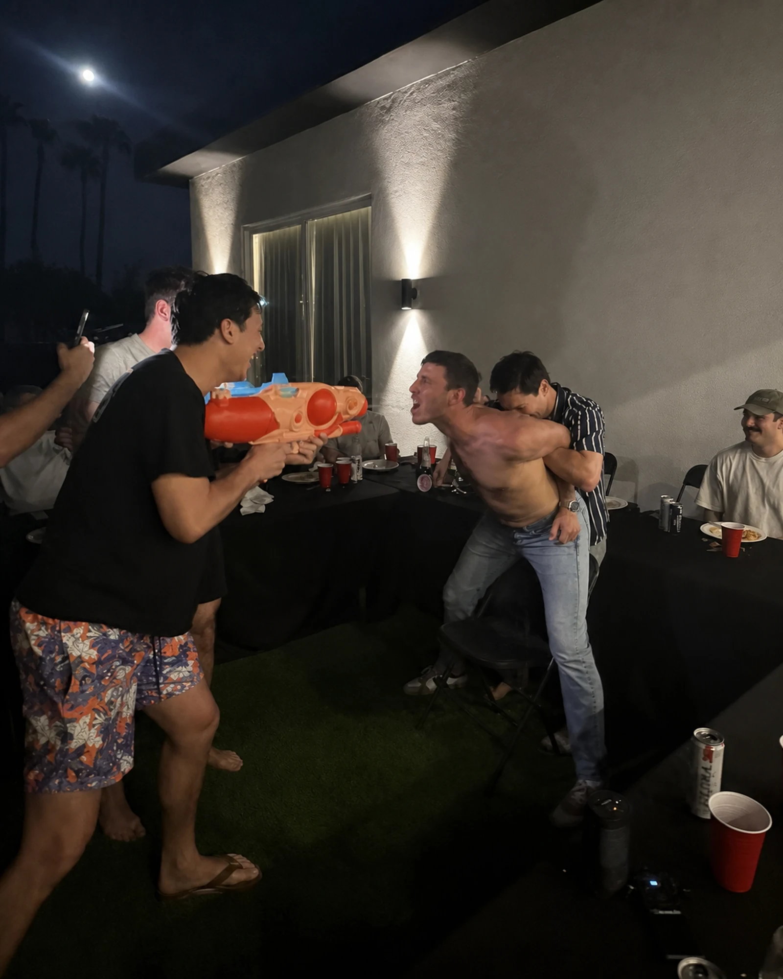 Guests laughing during an interactive water-gun moment at a backyard hibachi party
