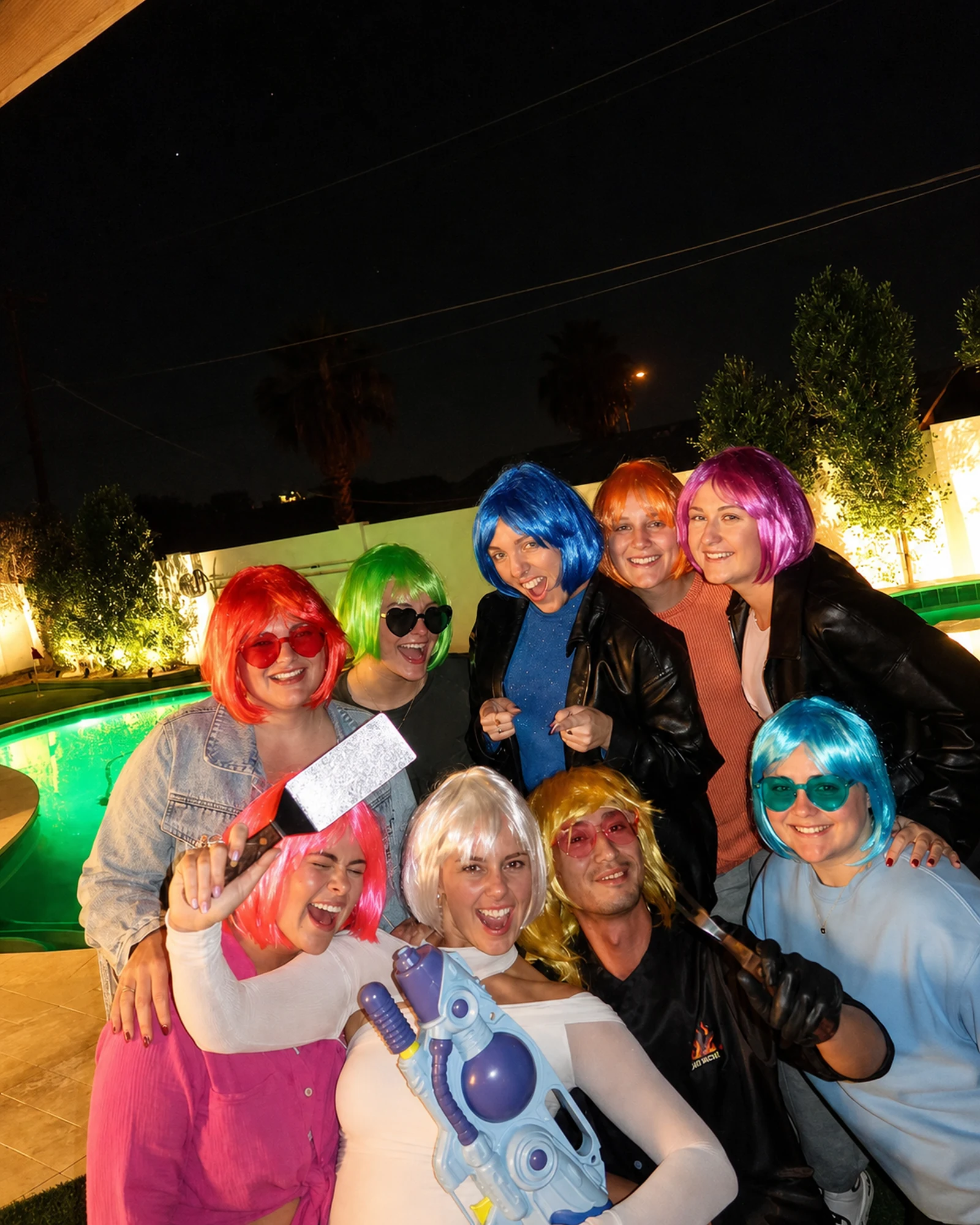 Bachelorette guests wearing colorful wigs during a nighttime pool party