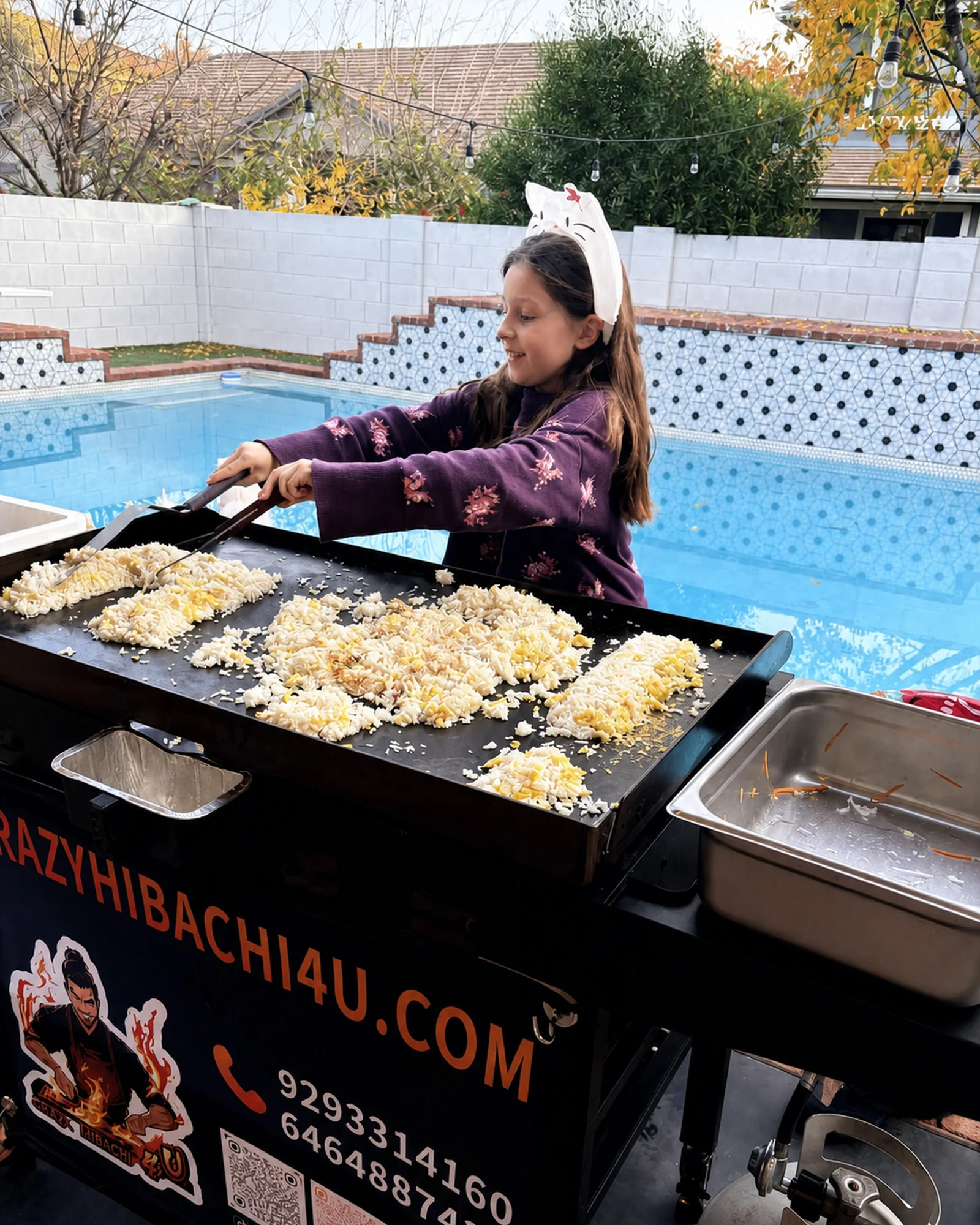 Child stirring fried rice on the outdoor grill with the hibachi chef nearby