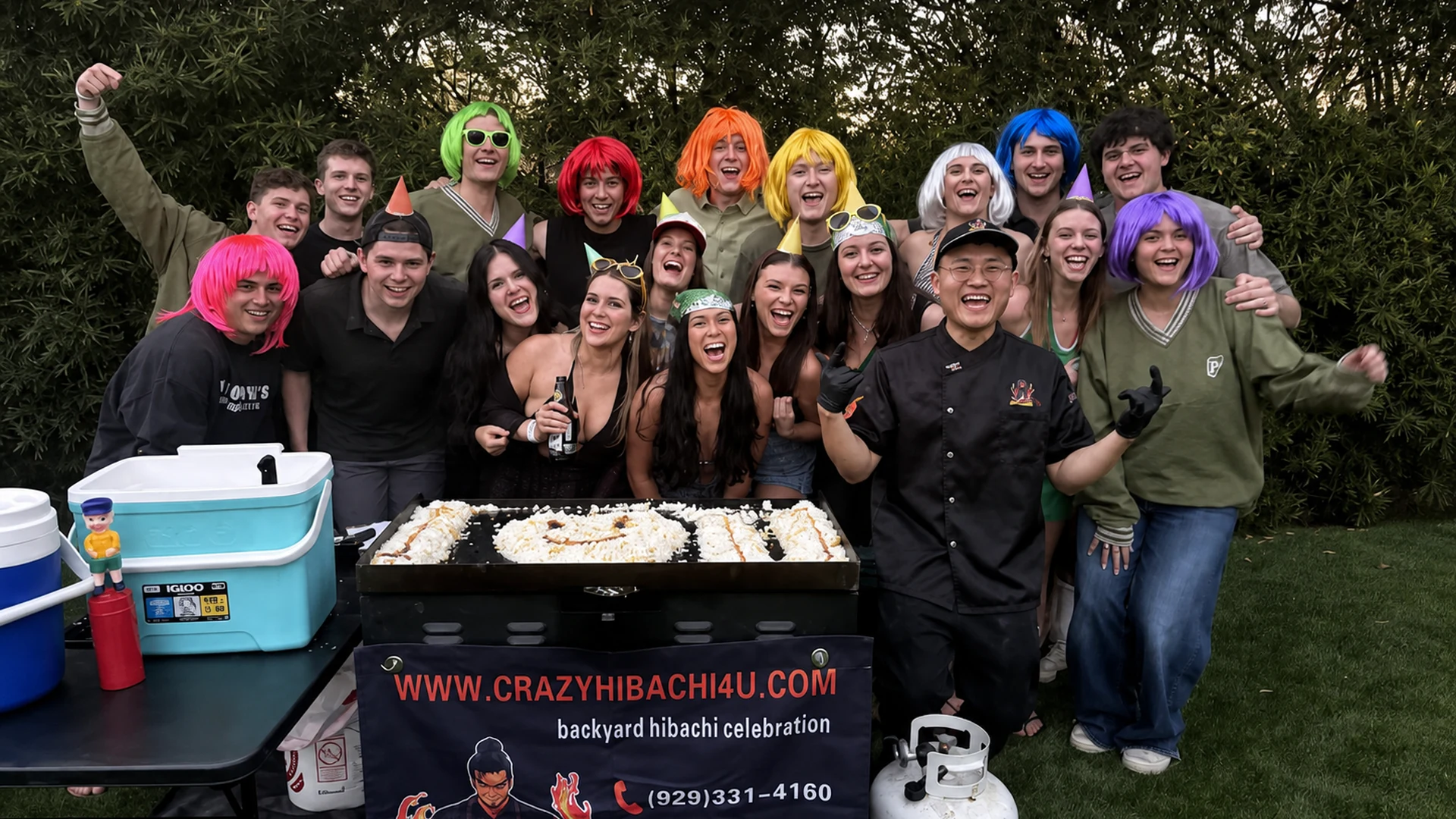 Large bachelorette group in colorful wigs posing with the hibachi chef and grill