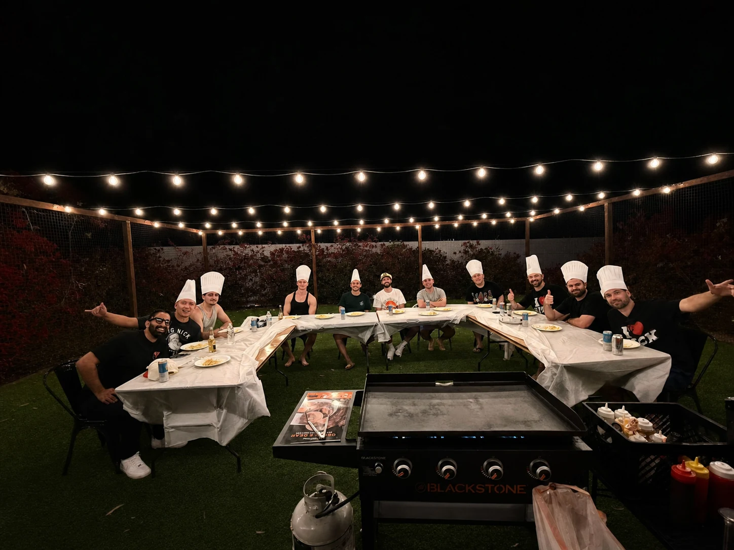Hibachi chef wearing a playful hat beside guests at a nighttime dinner