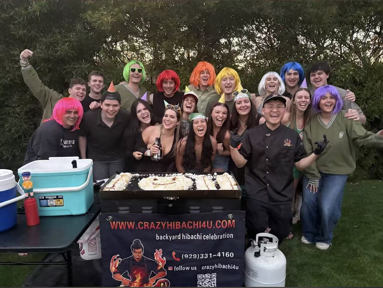 Hibachi chef and party guests wearing colorful wigs beside the grill
